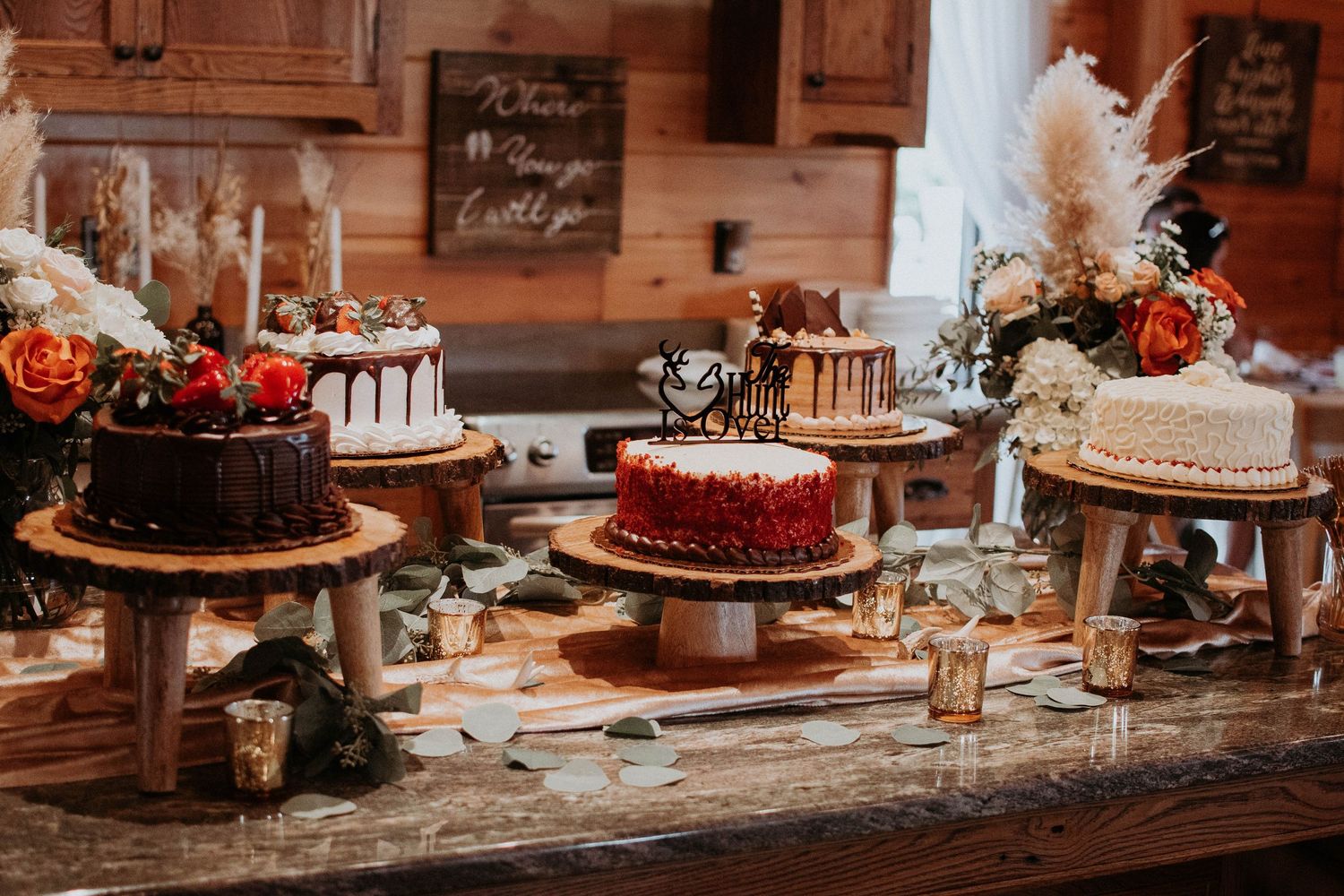 Rustic dessert table display featuring multiple wedding cakes on wooden stands with floral decorations.
