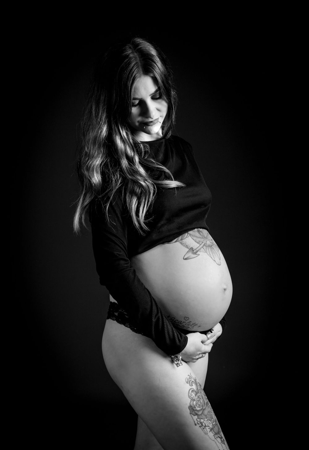 pregnant lady with black crop top looking down at bump photo is black and white