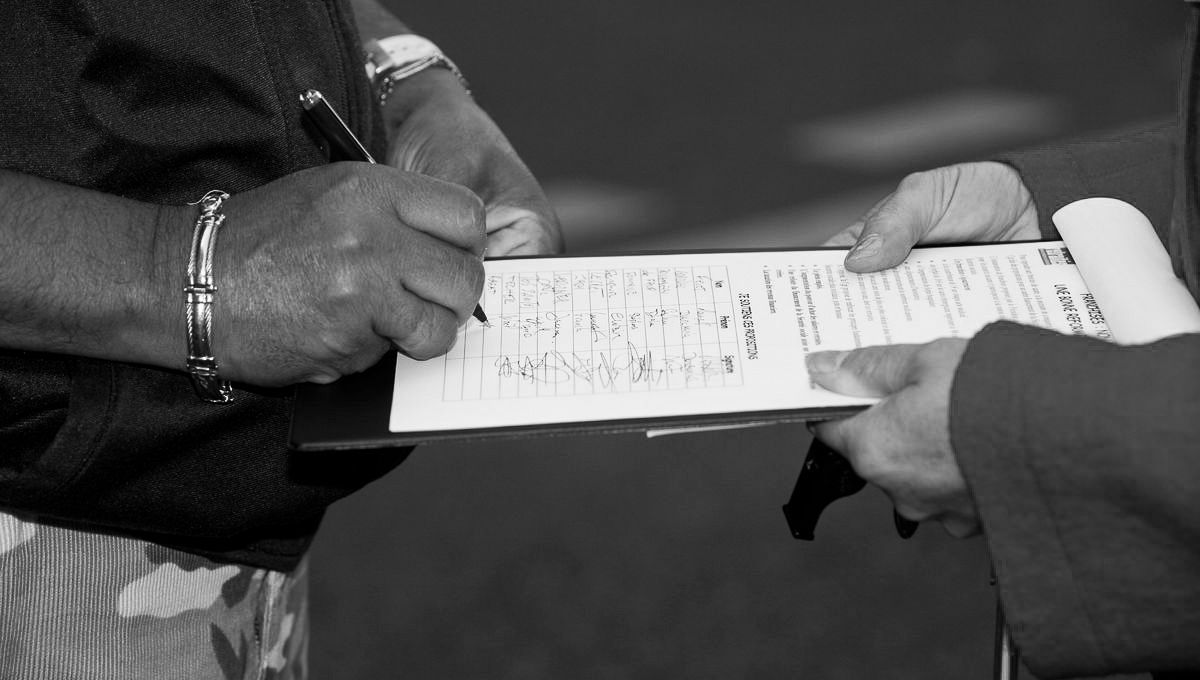 Close-up black and white image of hands filling out paperwork.