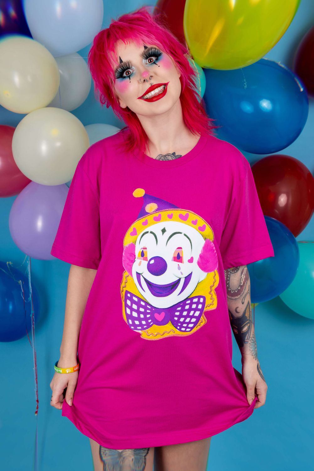 Alternative pink haired white model wearing clown makeup in front of a balloon background for small fashion brand.