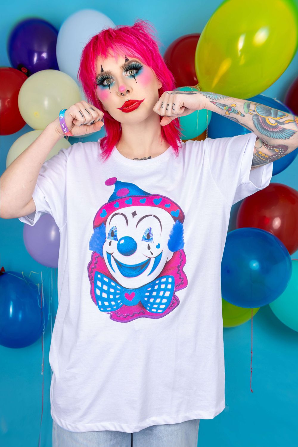 Alternative pink haired white model wearing clown makeup in front of a balloon background for small fashion brand.