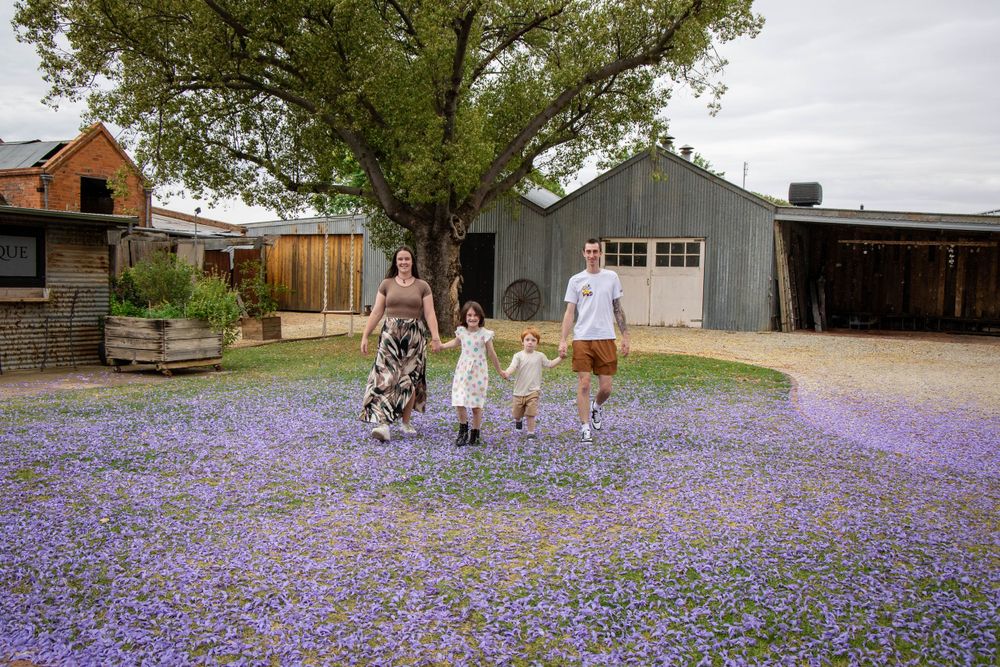 A rustic farmyard filled with blooming purple flowers surrounds a group walking together.