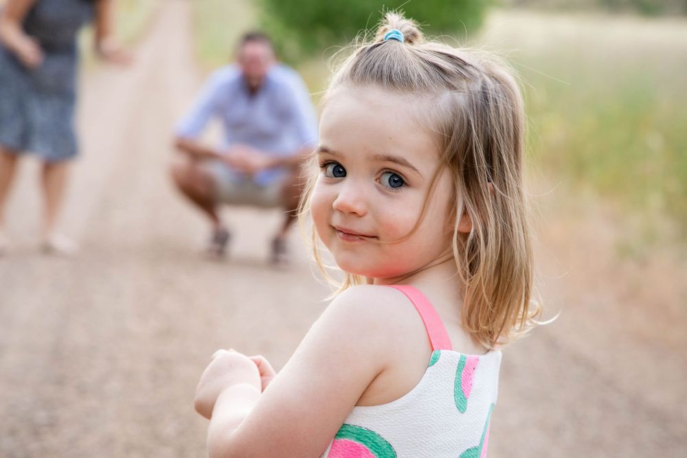 A child in a colorful summer dress looks back at the camera on a dirt path.