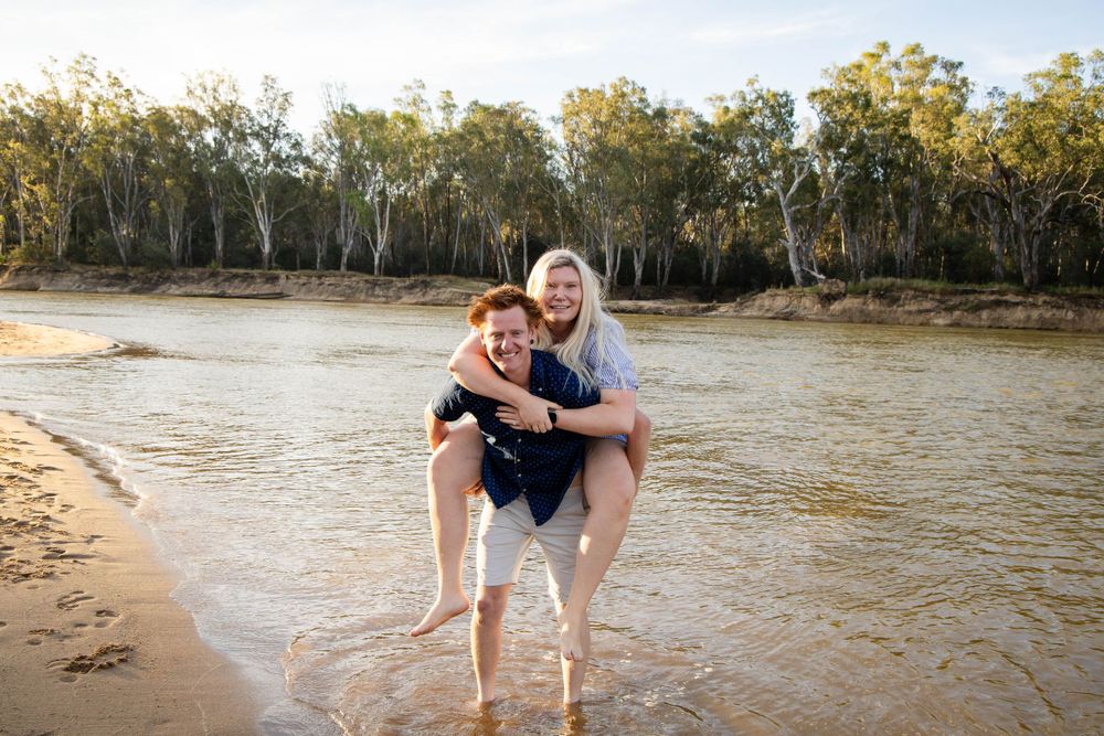 A playful moment captured on a sandy riverbank with trees in the background.