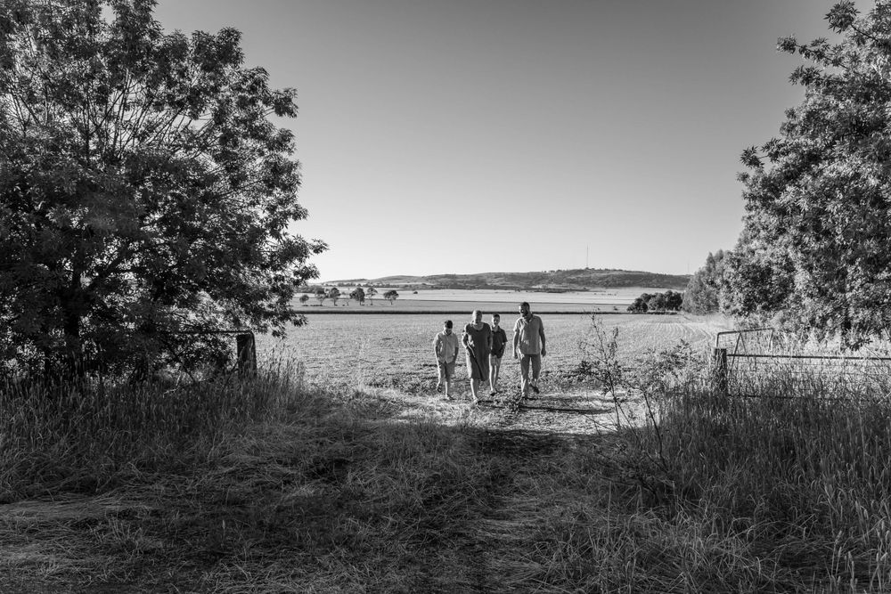A black and white landscape photo shows silhouettes walking along a rural path.