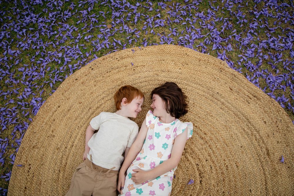 Two children lying on a hay bale surrounded by purple wildflowers.