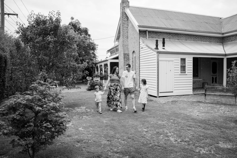 A vintage black and white photo of people walking outside a white farmhouse.