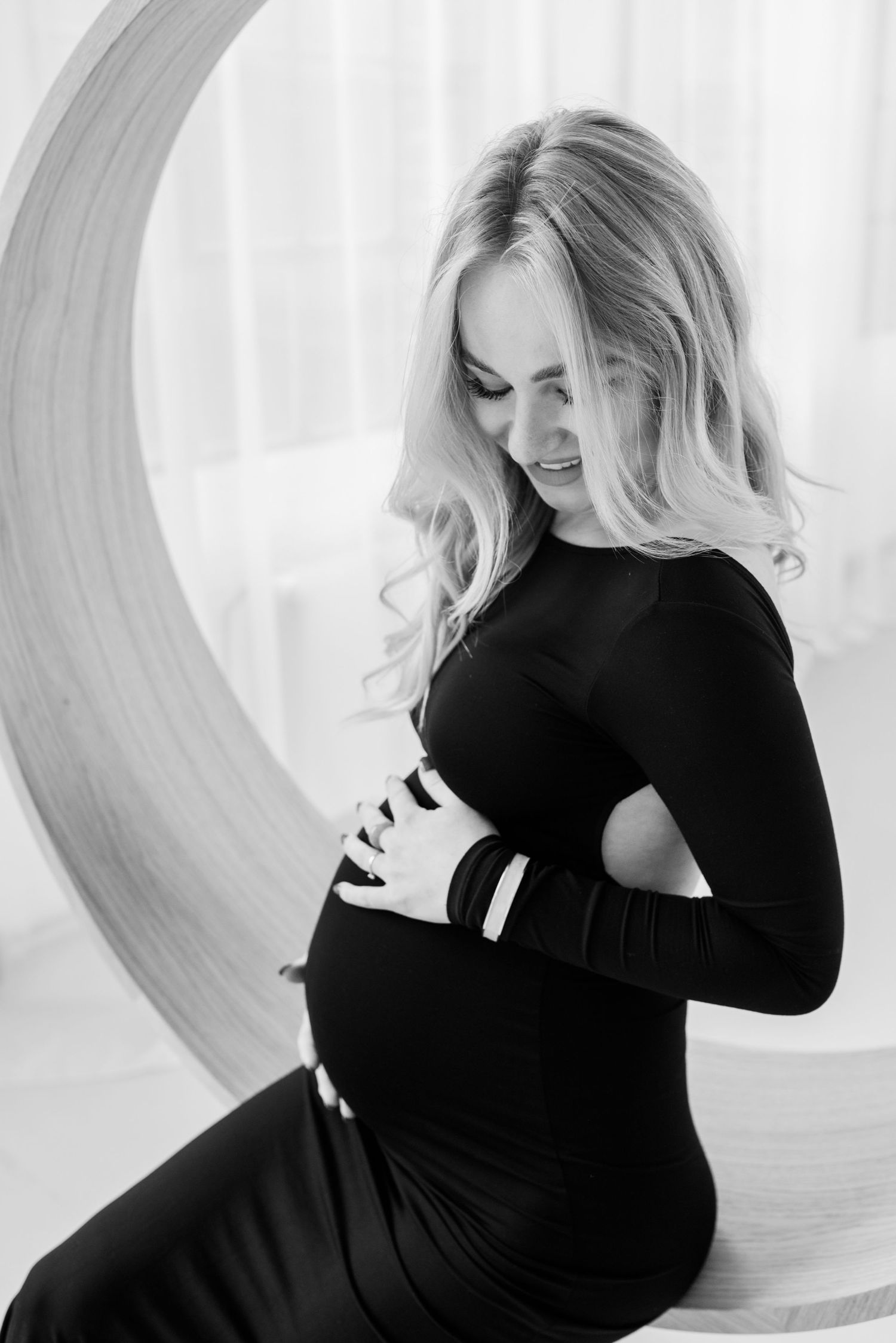 Black and white artistic portrait series of a woman in a black dress posing against a curved white background.