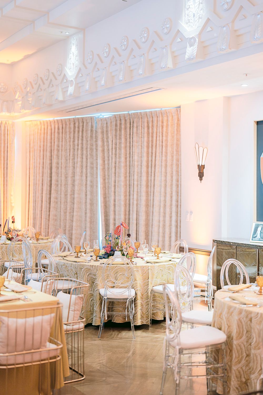 Elegant wedding reception room with white and pink decor, chandeliers, and round tables set for a formal celebration.