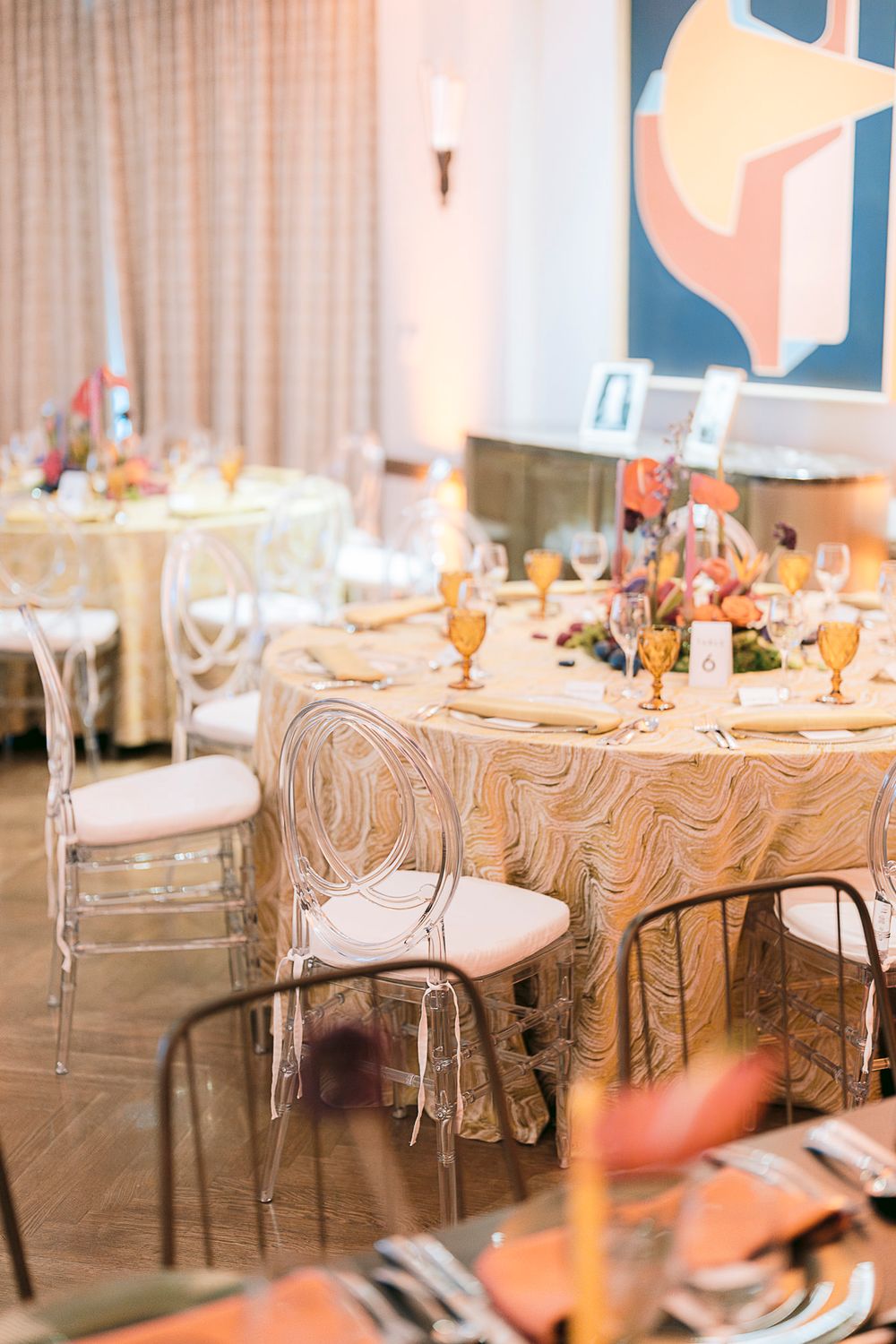 Elegant wedding reception setup with marble-patterned tablecloths, clear ghost chairs, and soft peach accents for decor.