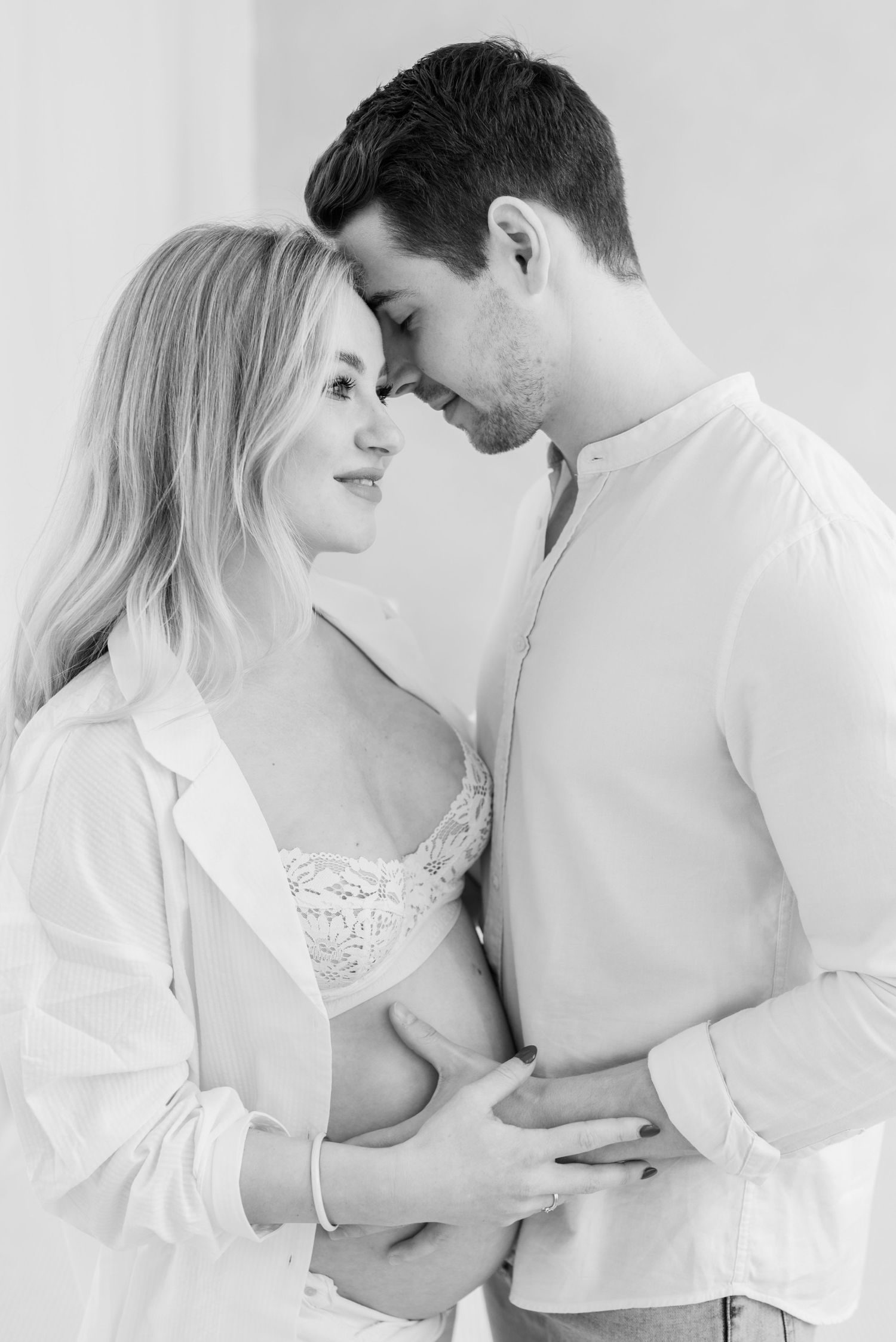A romantic black and white intimate portrait of a couple in white clothing sharing a tender moment together.