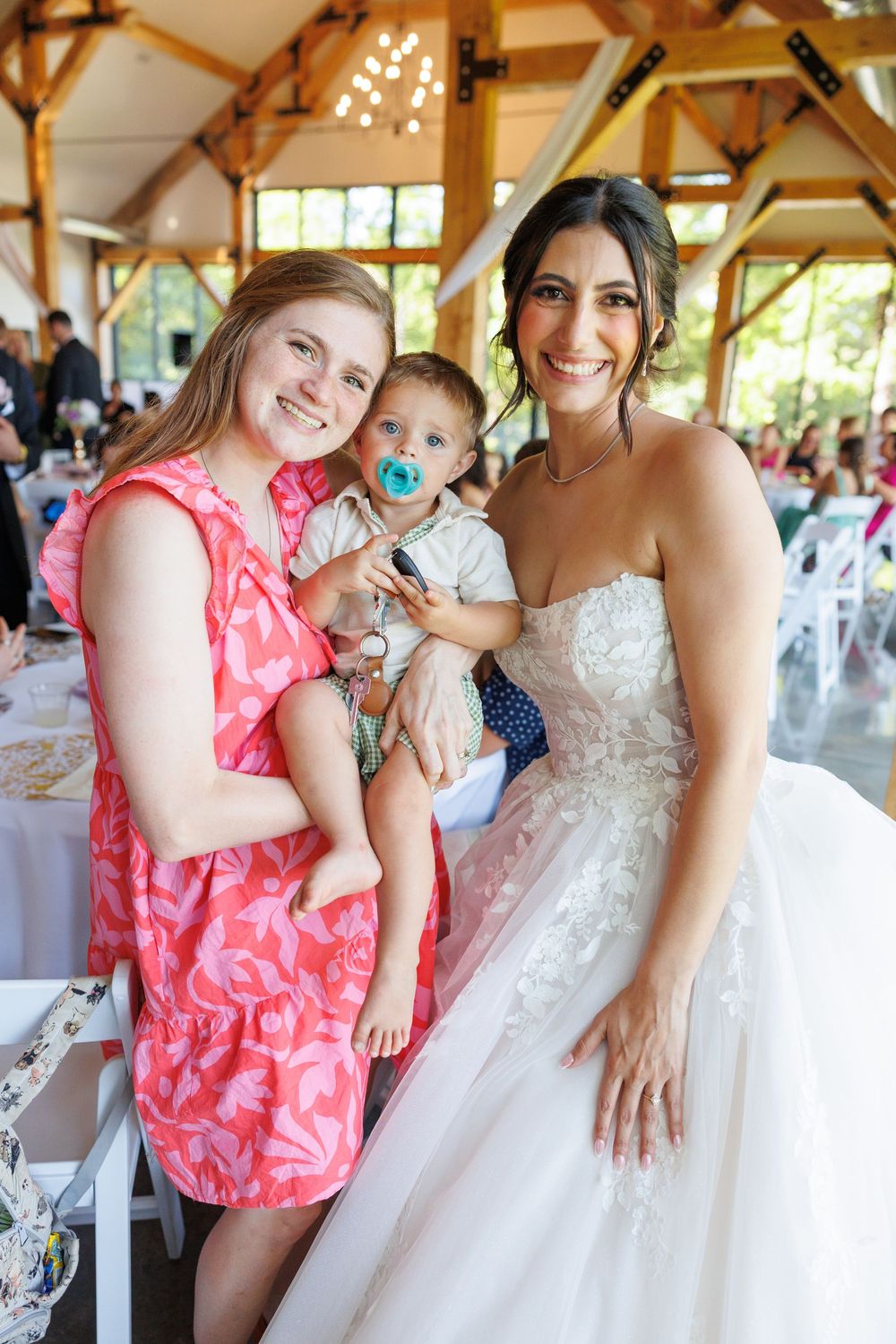 A bride in a white wedding gown shares joyful moments with a small child wearing a pink tropical print dress.