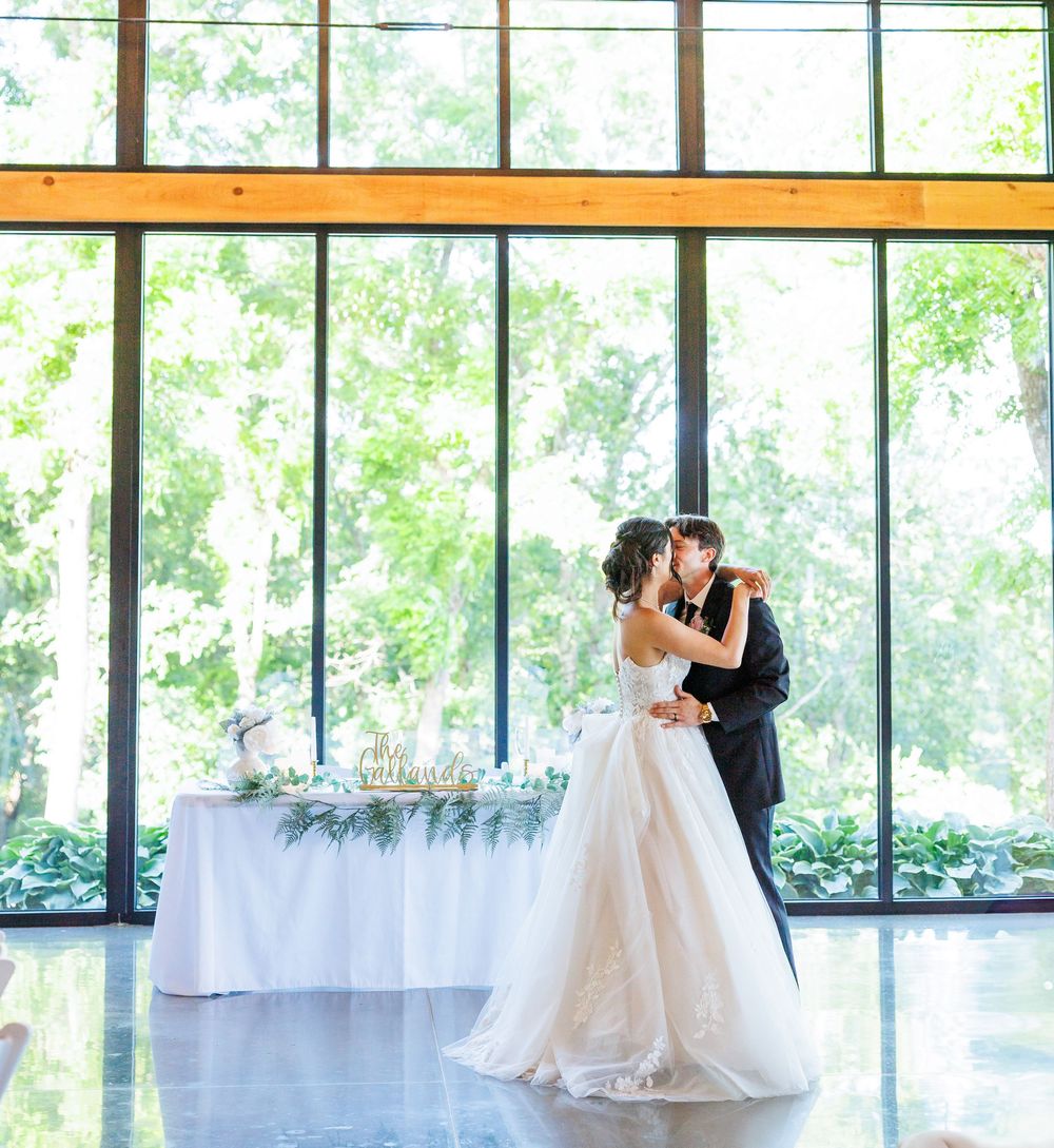 A couple shares an intimate dance in a sunlit venue with floor-to-ceiling windows and white decor.