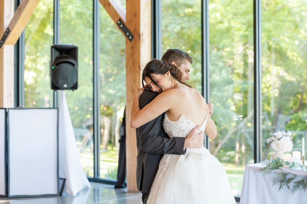 A couple shares their first dance at a wedding reception in a sunlit venue with floor-to-ceiling windows.