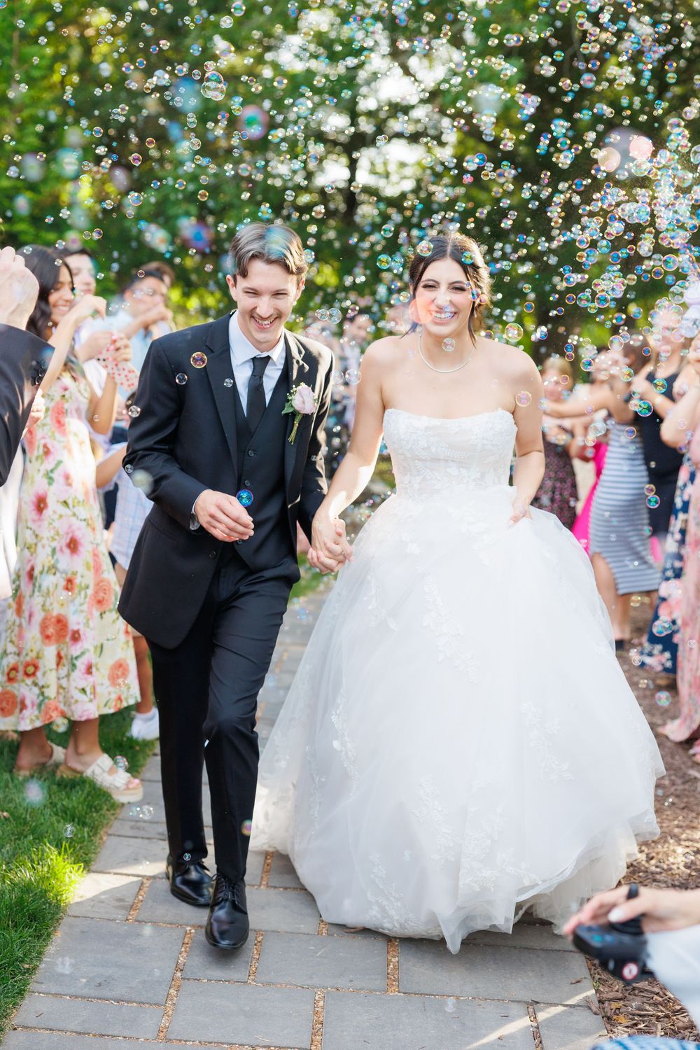 Wedding party throws white petals at a bride and groom walking down a garden path after their ceremony.