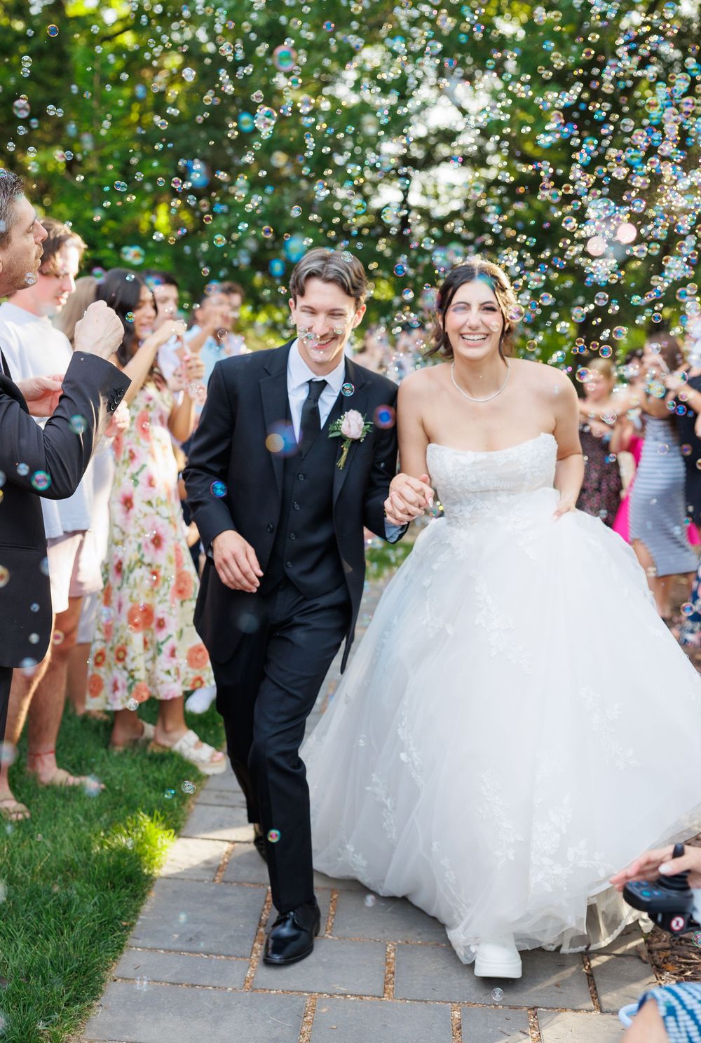 Happy couple walking through shower of bubbles at outdoor wedding ceremony as guests celebrate.