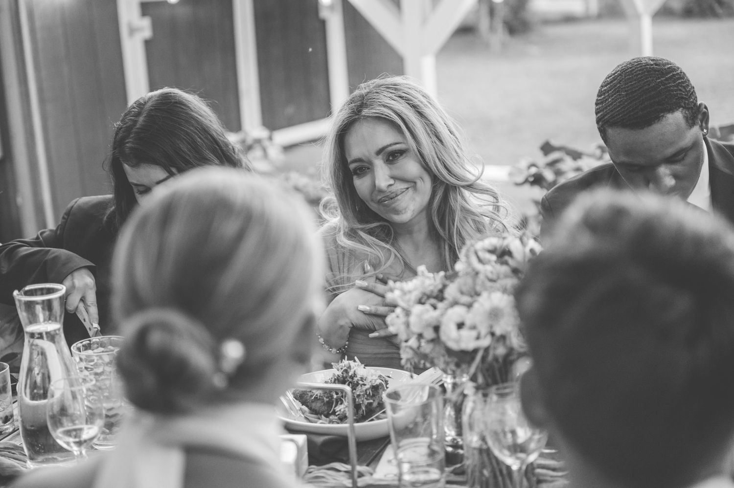 A black and white photo of guests enjoying a casual outdoor dining gathering with flowers on the table.
