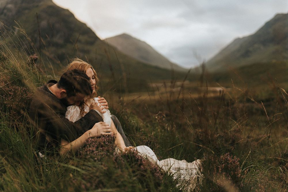 A couple sharing an intimate moment against a dramatic backdrop of rolling hills and mountains.