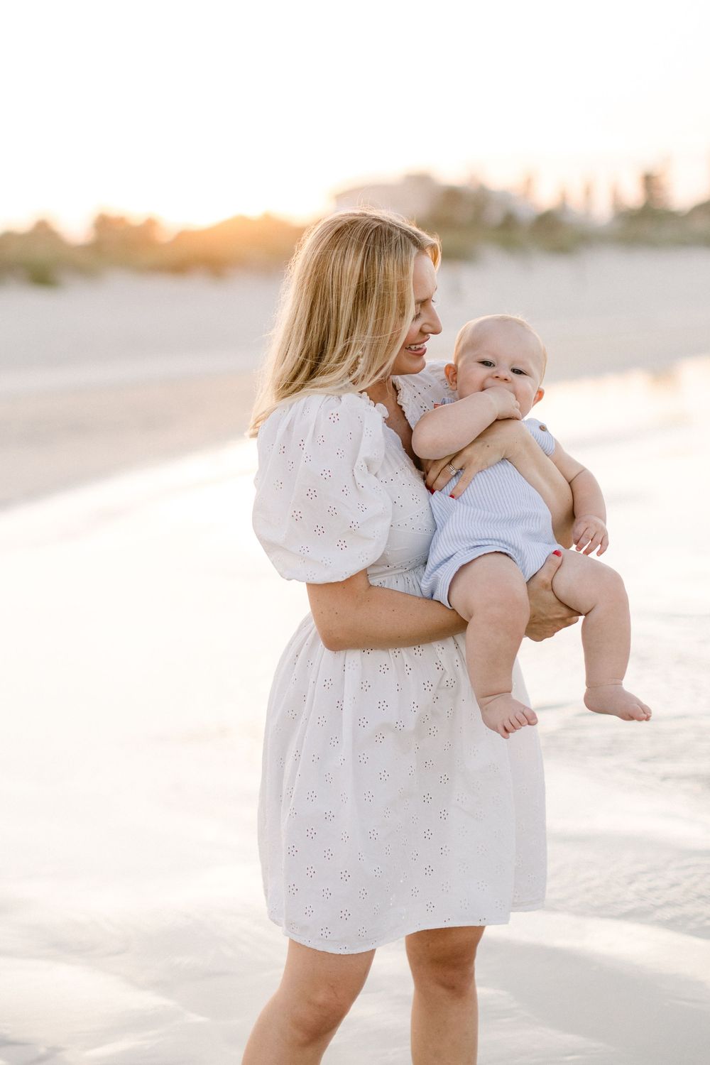 A tender moment between parent and baby on a sun-drenched beach with soft white sand at golden hour.