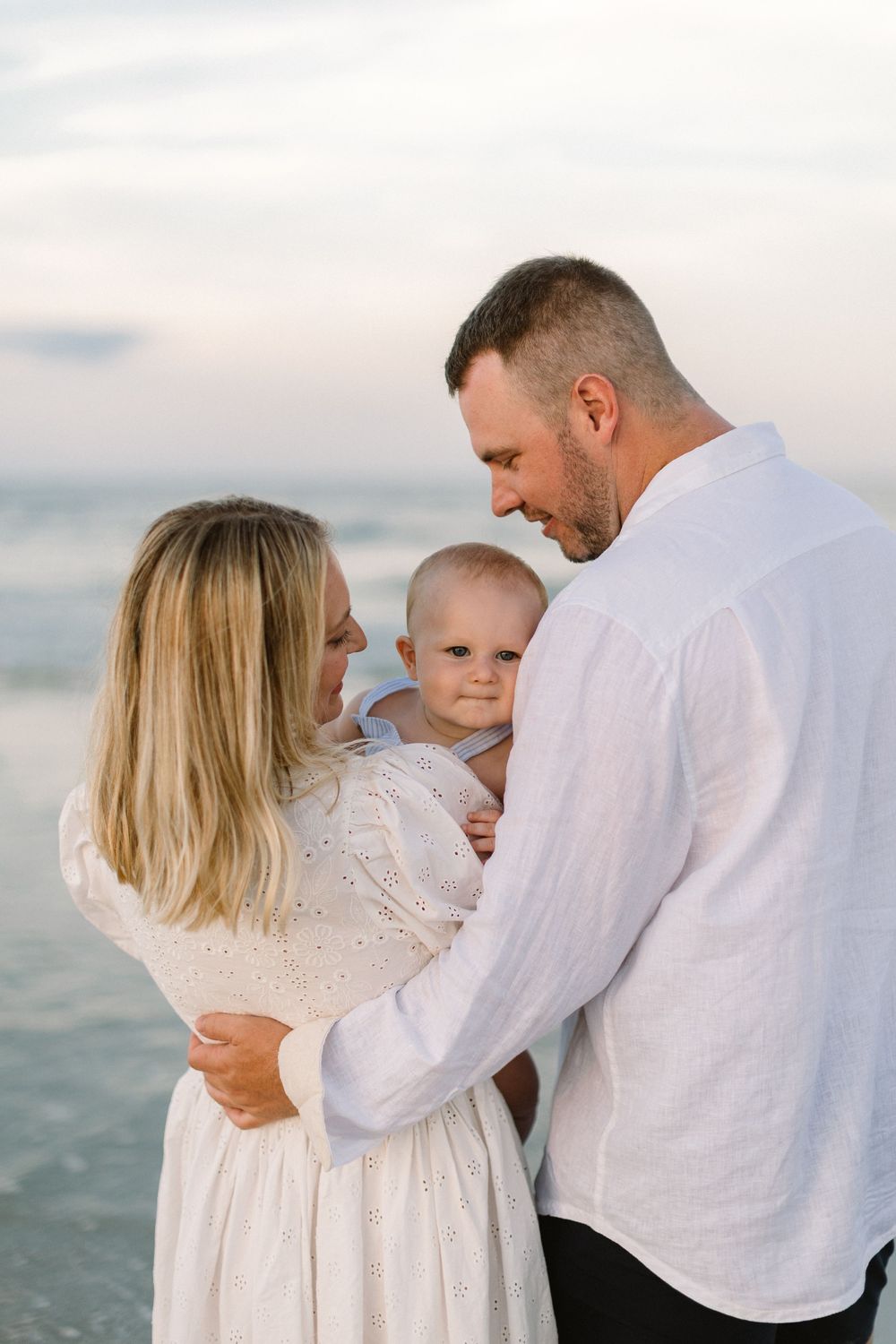 A family dressed in white embraces together on a peaceful beach at sunset.