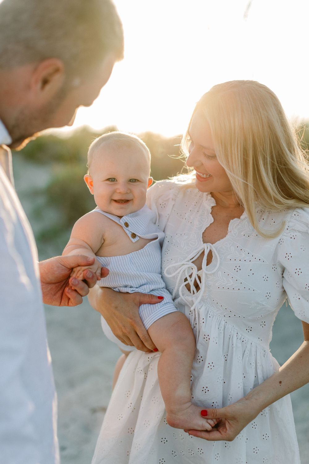 Happy family enjoying a tender moment together on the beach at sunset in white summer outfits.