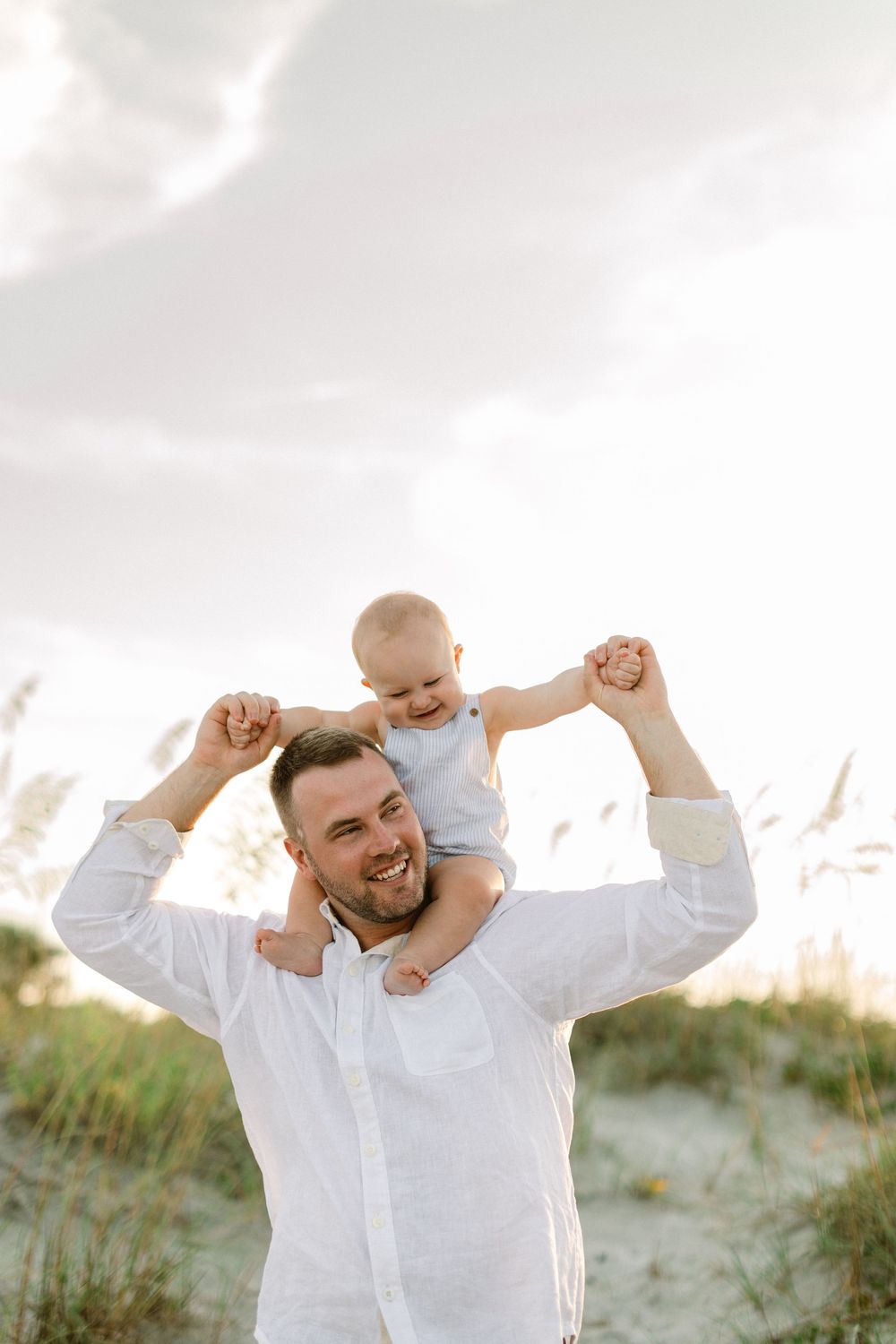 A parent and baby share a joyful moment together on sand dunes during a bright summer evening.