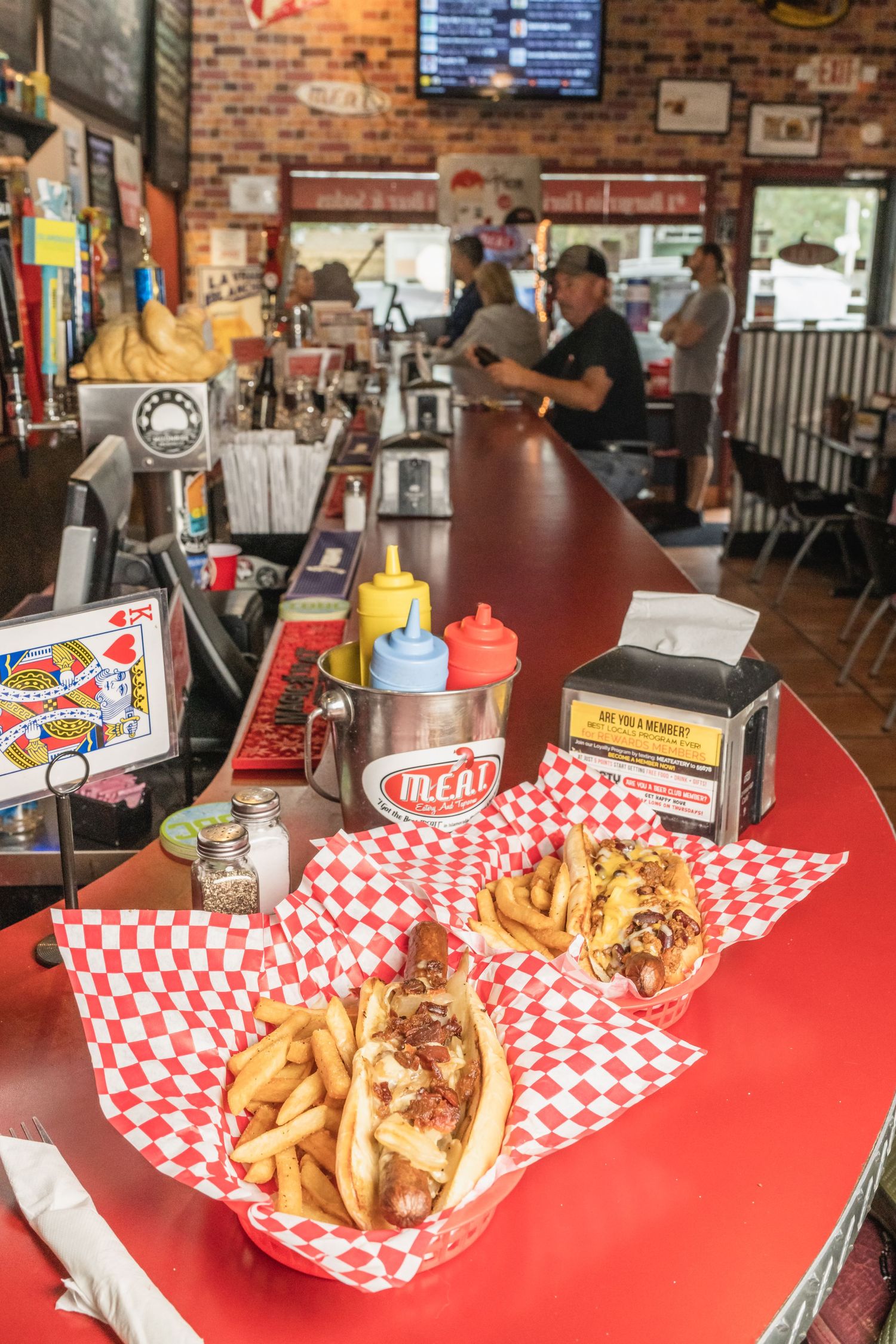 Classic diner setting with loaded hot dogs and fries served in red checkered paper baskets on counter.
