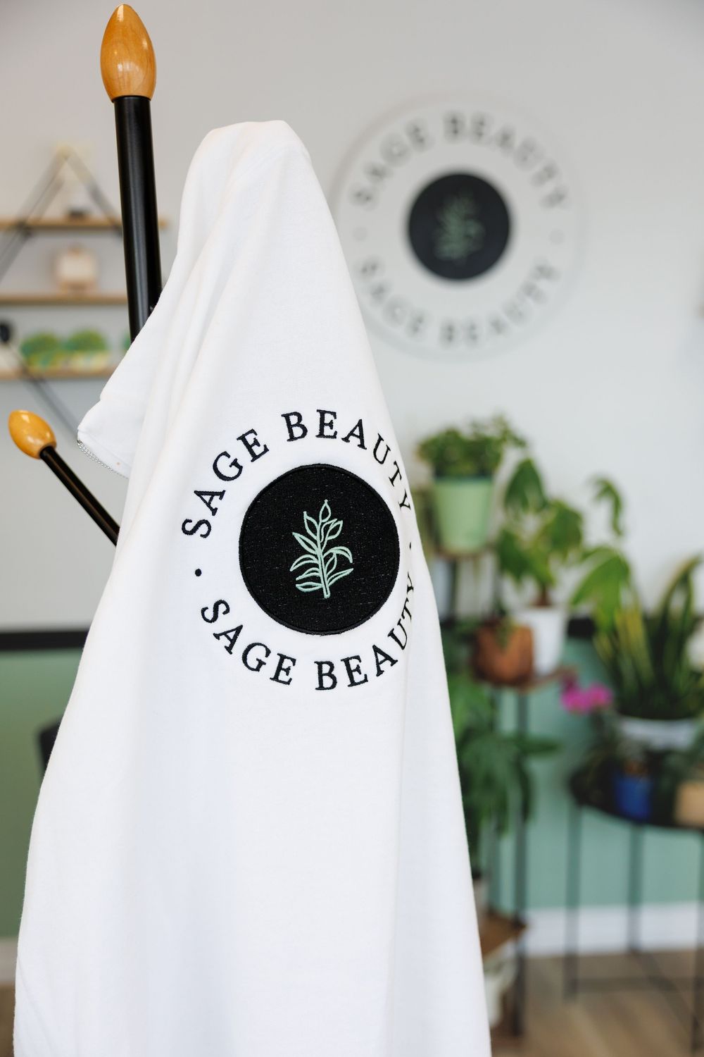 Close-up view of white clothing items featuring a black circular logo with sage leaf design at a retail display.