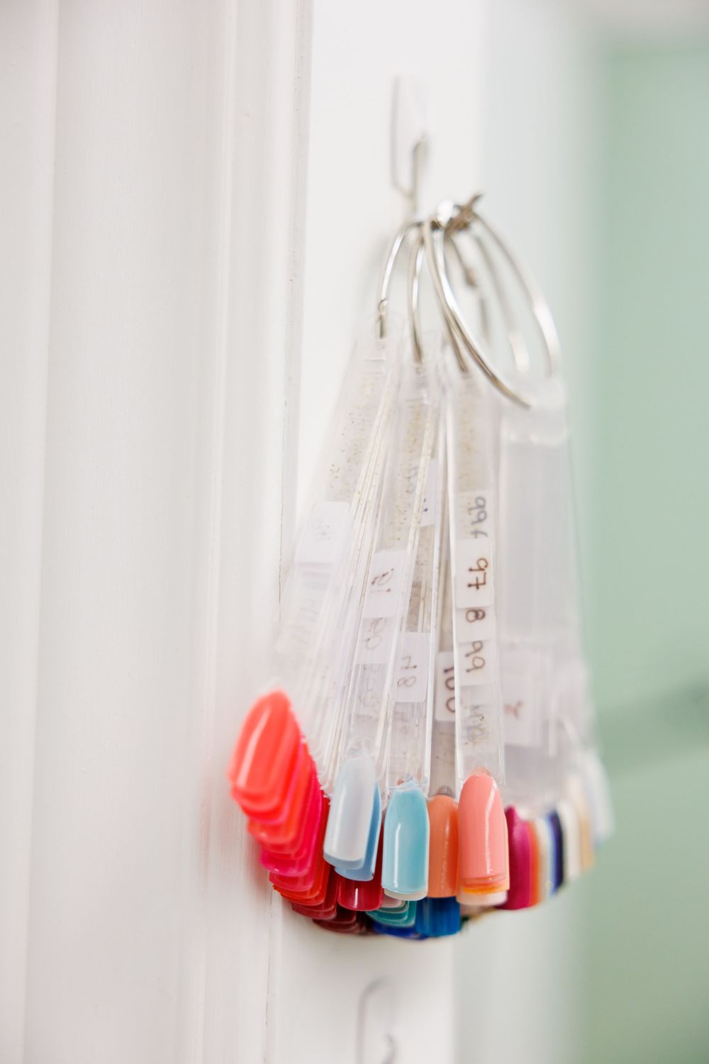 Colorful nail polish bottles hanging in a clear plastic organizer against a white wall.