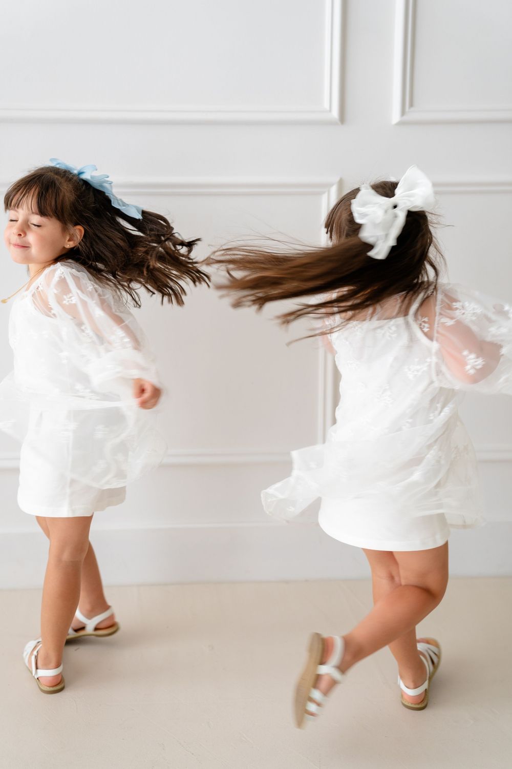 Young child in a white dress twirls and dances playfully on a white floor.