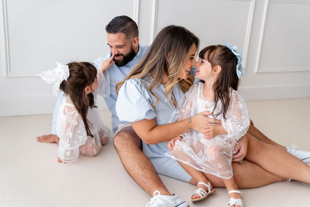 People sitting together on a light colored floor in intimate poses, wearing casual attire in a bright interior.