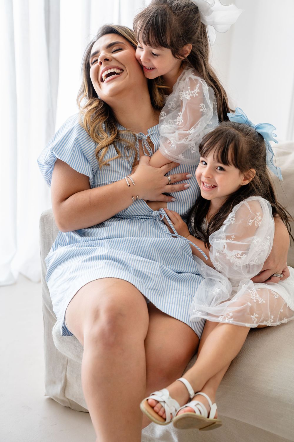 Two figures sharing joyful embraces and laughter on a bright white couch with soft window light.