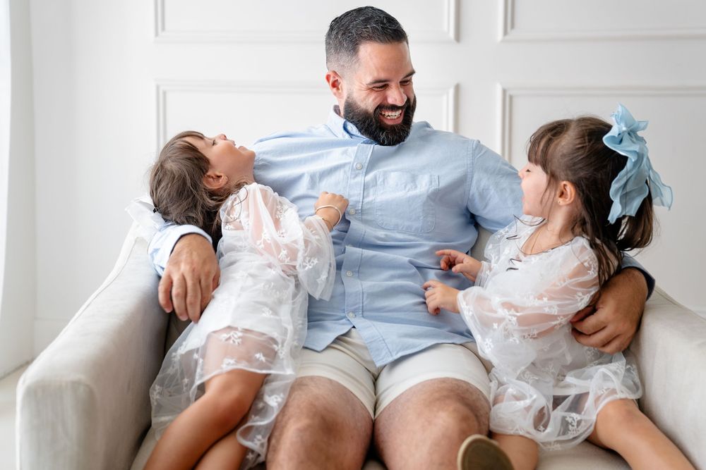 Three people sit together and laugh while sharing a tender moment on a light-colored sofa.