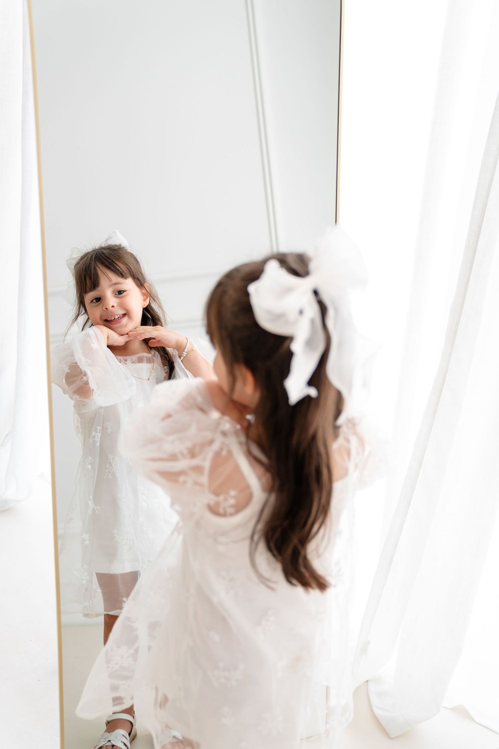 Dancing and twirling in a flowing white dress against sheer curtains in natural light.