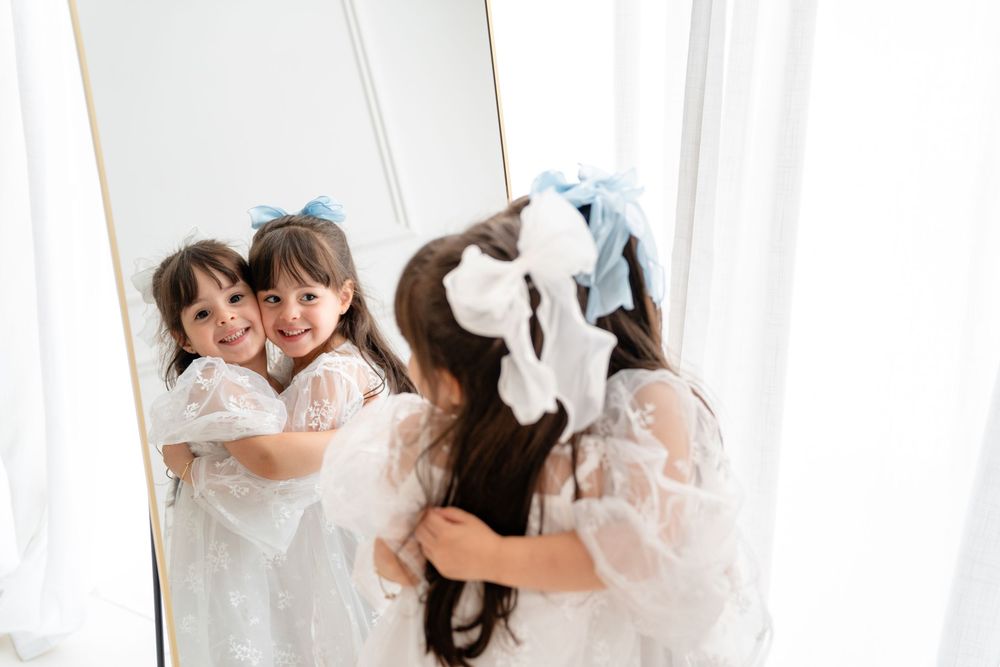 A playful interaction between someone wearing white and a mirror reflection in a bright interior setting.