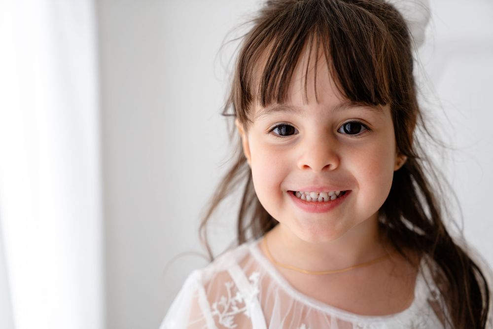 A bright indoor portrait against a white background wearing a delicate lace dress.