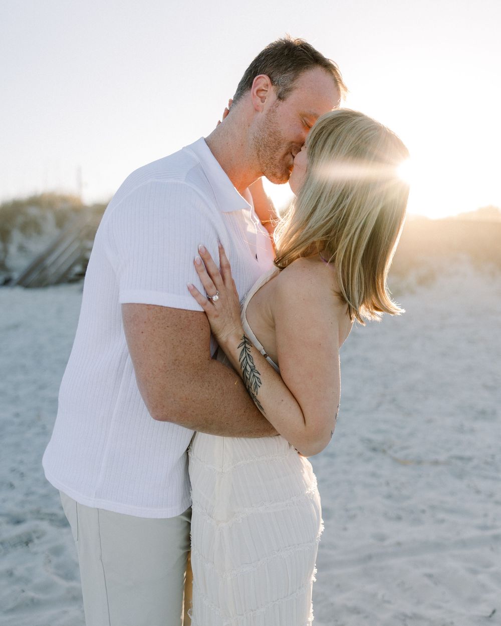 A tender beachside moment between a couple in white outfits during golden hour.