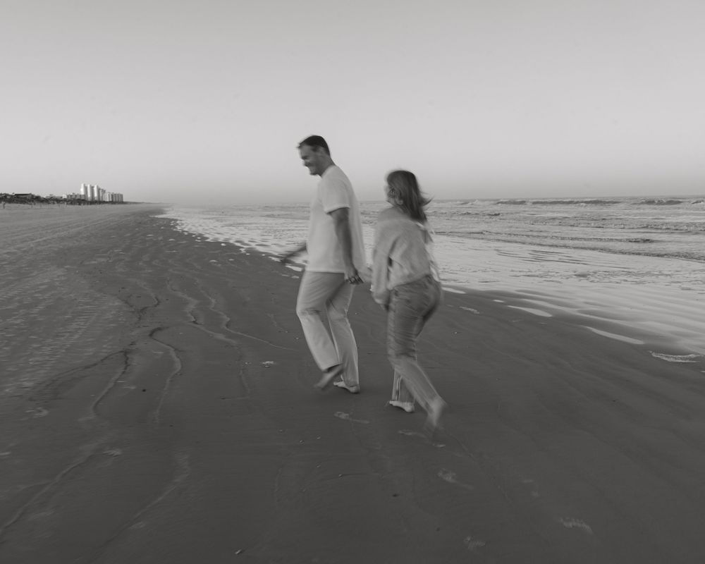 A couple walks together on a sandy beach in black and white photography.
