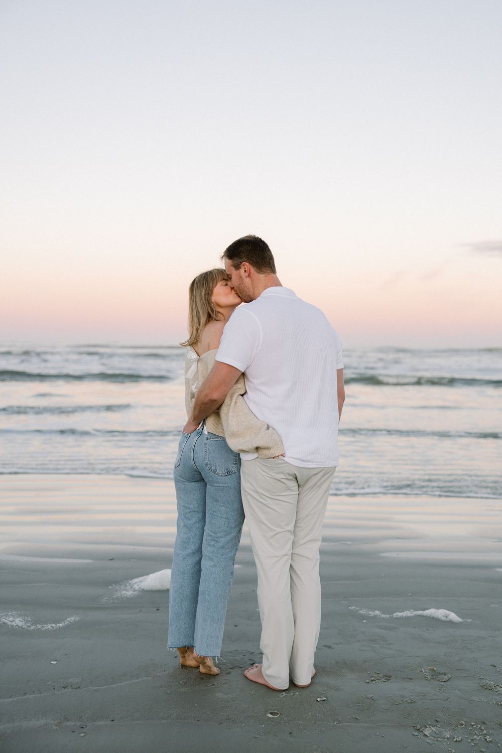 A couple stands close together watching the sunset on a peaceful beach.