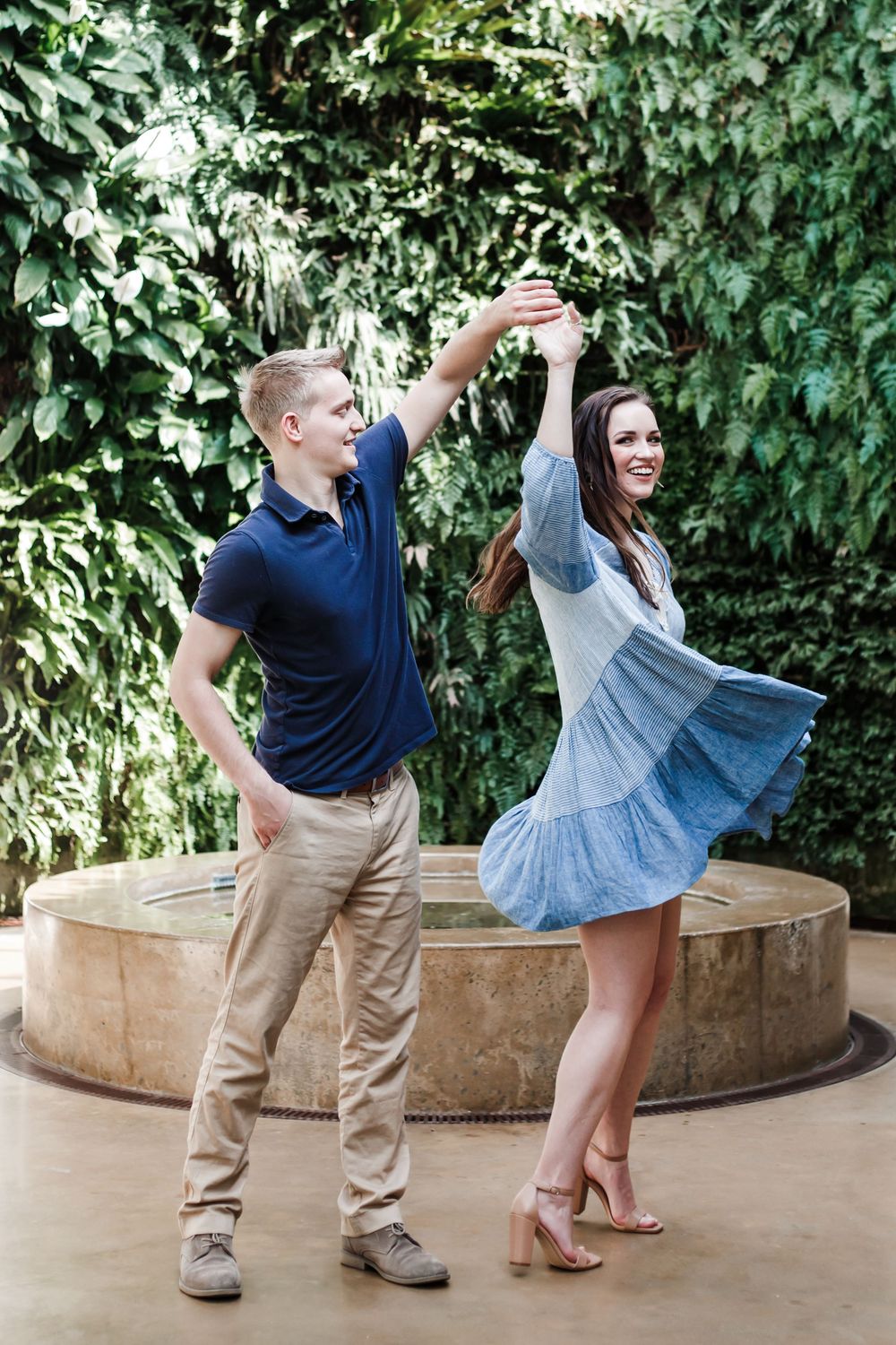 Couple dancing joyfully together in front of an ivy-covered wall, with the woman wearing a flowing blue dress.