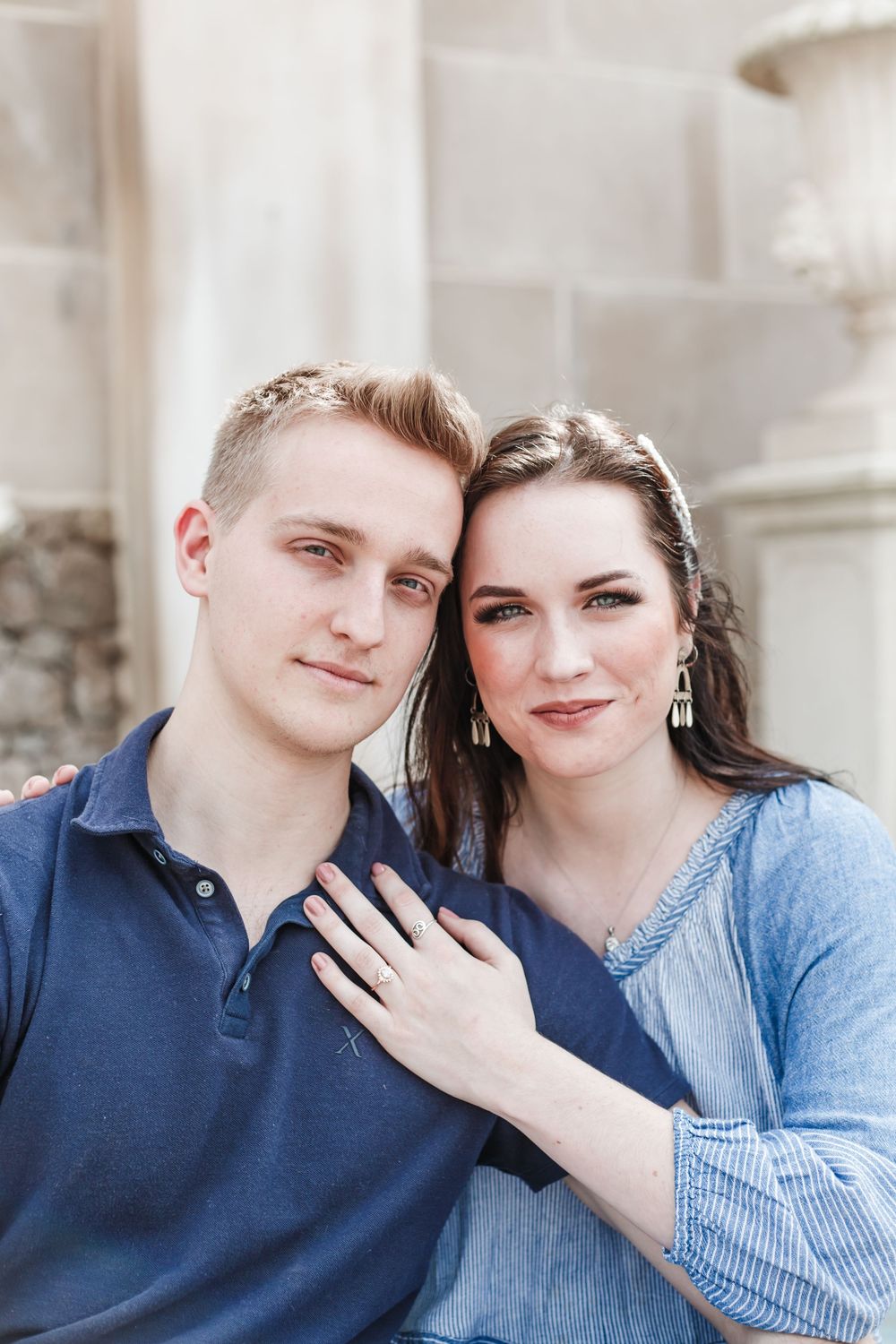 A romantic portrait of a couple in blue outfits against a light stone wall background.