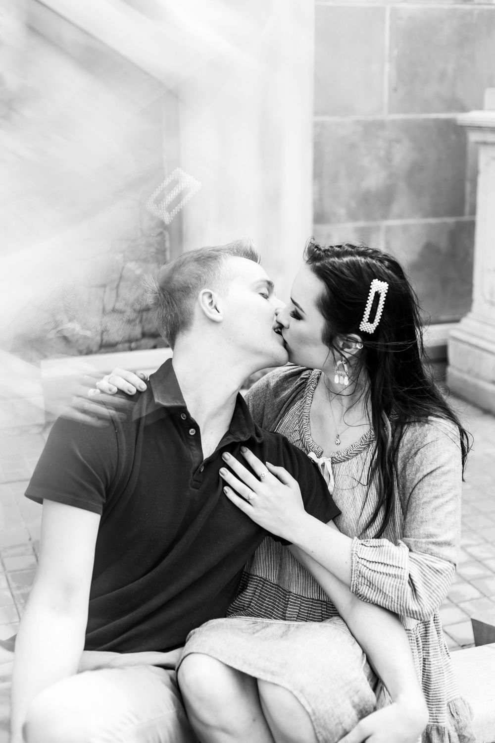 An intimate black and white portrait of a couple sharing a tender kiss while sitting together.