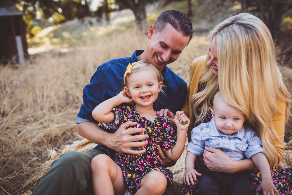 A young family sits together in a golden field during sunset, sharing joyful laughter and embraces.