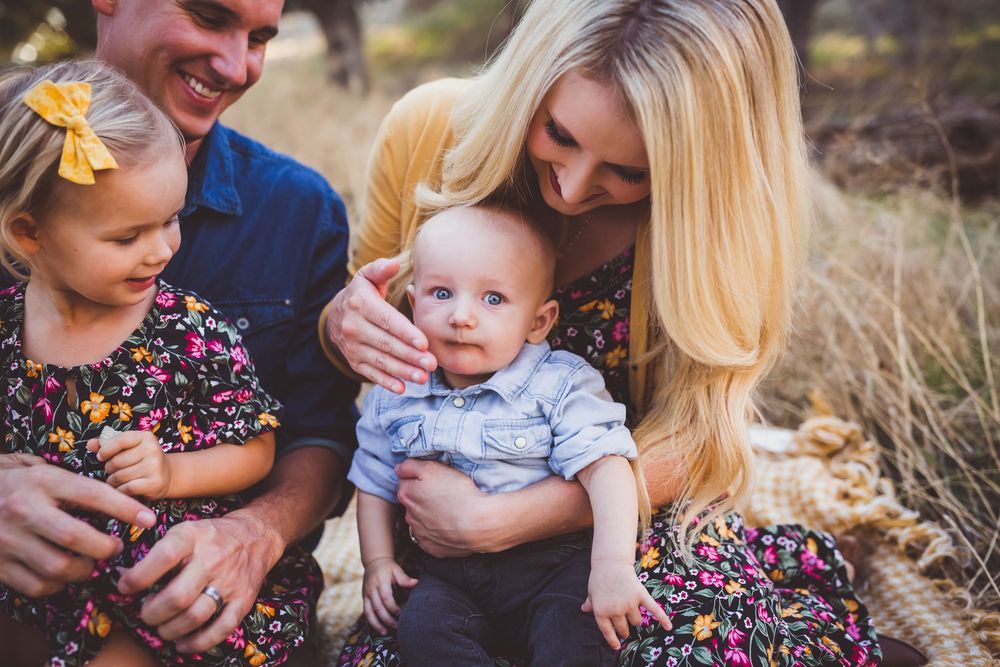 A family sits together outdoors in nature during a lifestyle photo session wearing coordinated casual outfits.