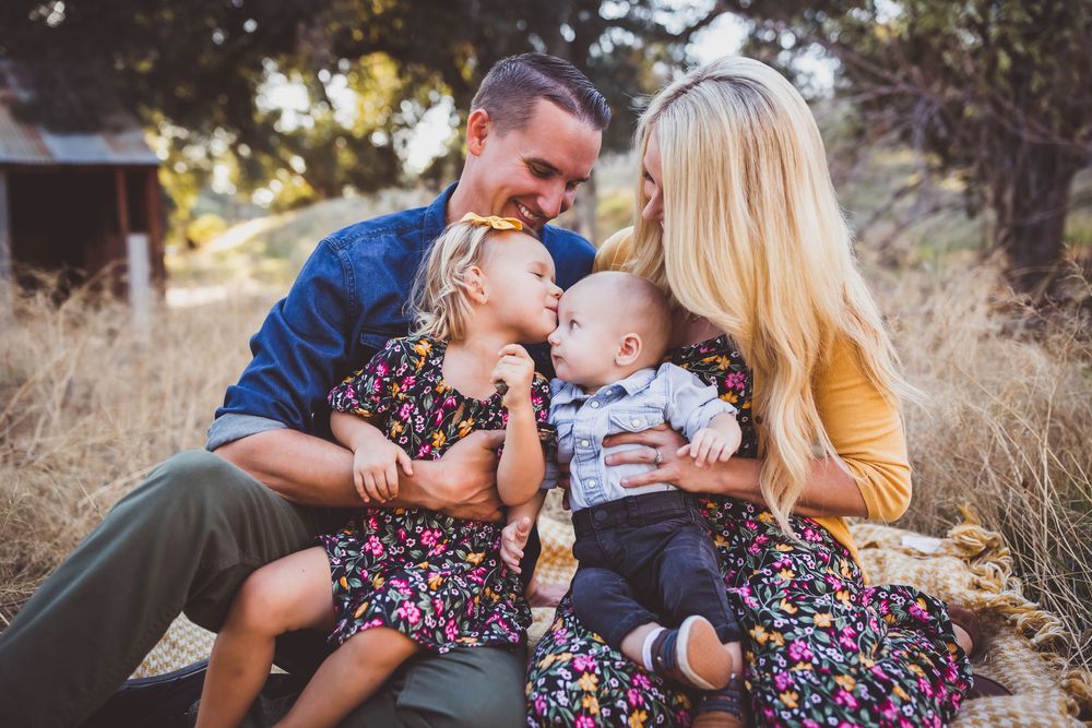 Family shares tender moments together on grassy hillside during sunset photo session.
