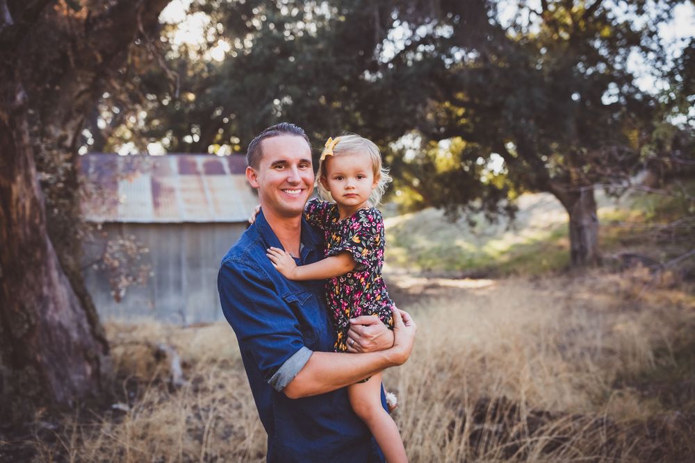 A joyful moment captured between adults and children in casual attire against a natural outdoor backdrop at sunset.