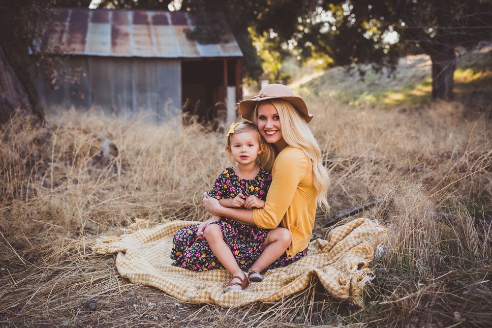 Tender moment shared on picnic blanket near old barn in tall grass at golden hour.