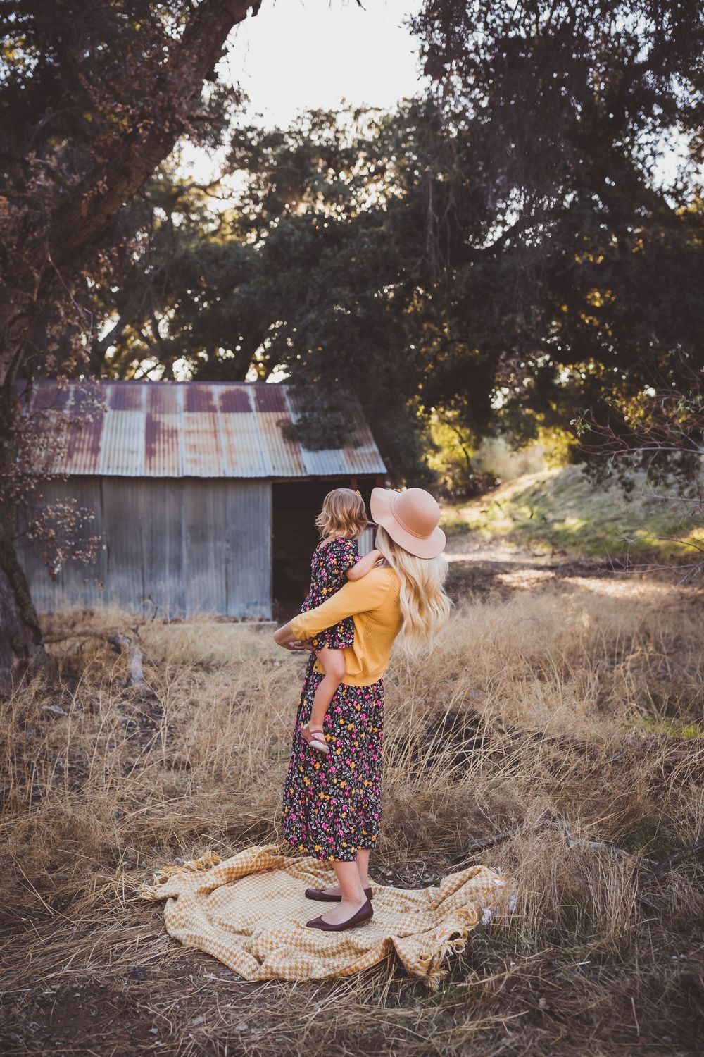 Joyful twirling dance on blanket near rustic barn surrounded by dry grass and trees.