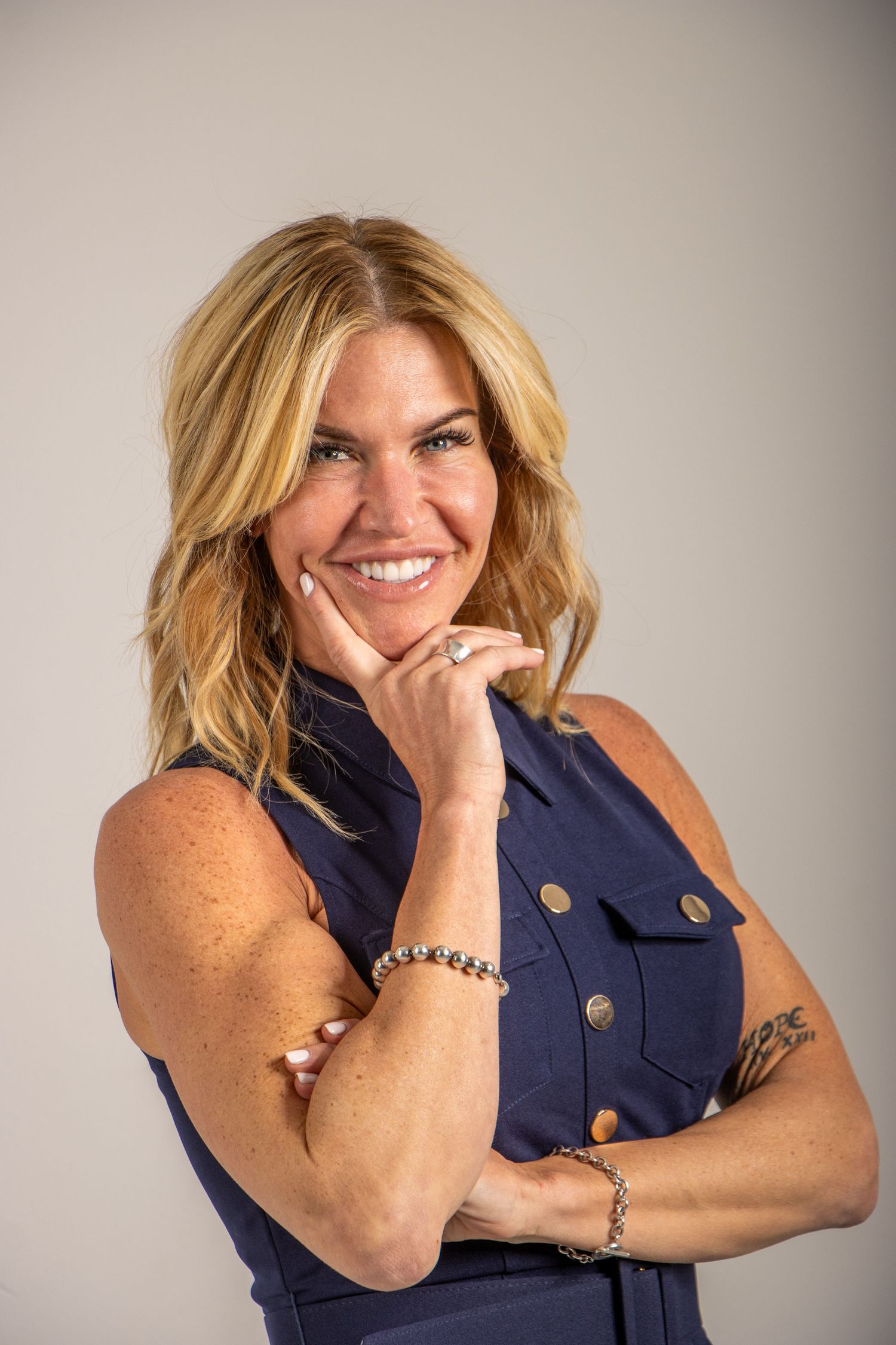 Four professional headshots showing a blonde figure in a navy blue sleeveless top posing with hand gestures and warm smiles.