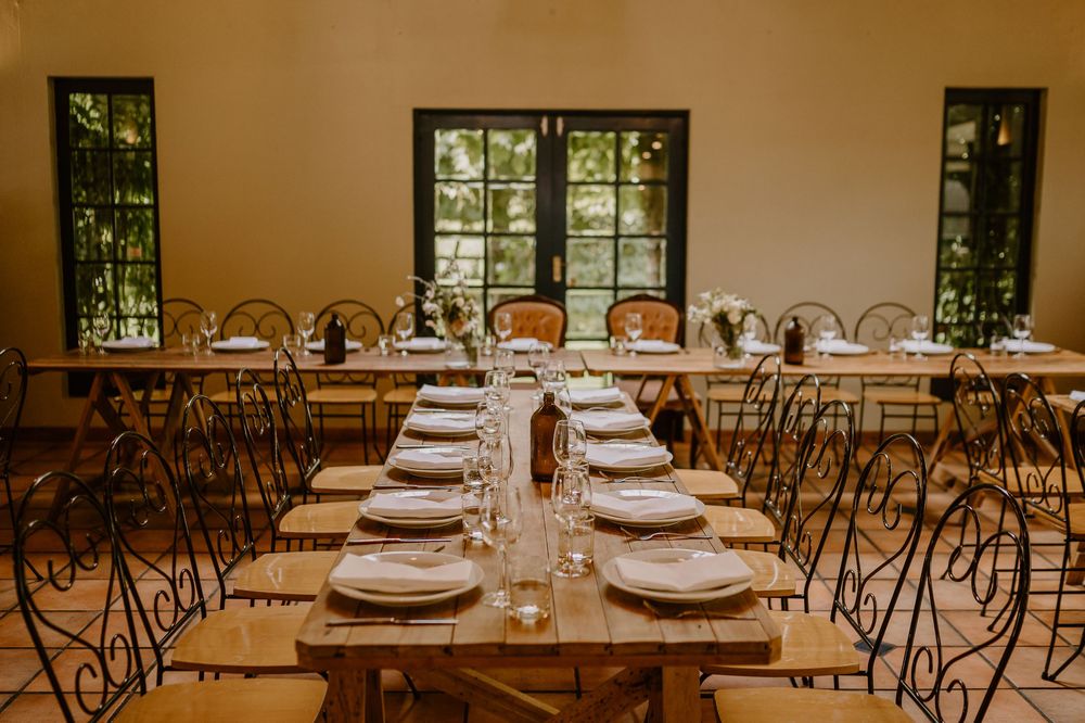 Elegant wedding reception table setup with vintage chairs and place settings in natural-lit room.